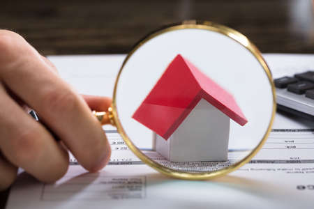 Close-up Of A Businessperson's Hand With Magnifying Glass Zooming On House Modelの写真素材