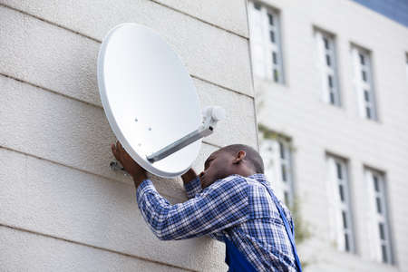 Young African Man In Uniform Fitting TV Satellite Dish On Wallの写真素材