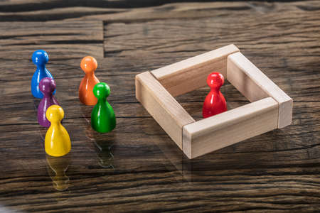 Red Figurine Pawn Separated By Wooden Blocks From Colorful Figurinesの写真素材