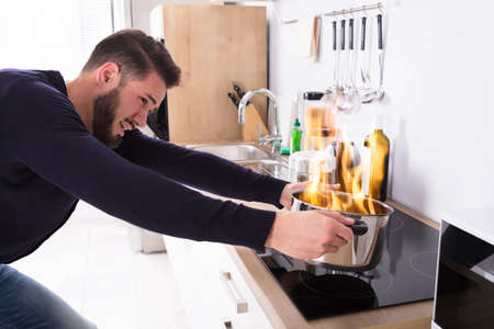 Side View Of A Young Man Holding Utensil On Fire In Kitchenの写真素材