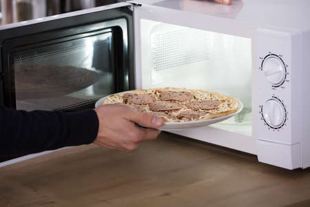 Close-up Of A Human Hand Baking Pizza In Microwave Ovenの写真素材