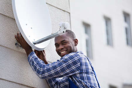 Young African Man In Uniform Fitting TV Satellite Dish On Wallの写真素材