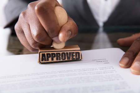 Close-up Of A Person's Hand Stamping On Approved Contract Form On Desk