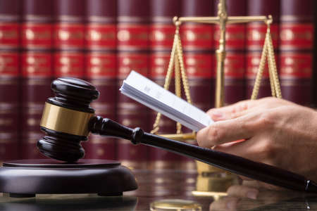 Close-up Of Gavel In Front Of Person's Hand Holding Document