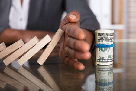 Close-up Of A Human Hand Stopping Wooden Blocks From Falling On Money