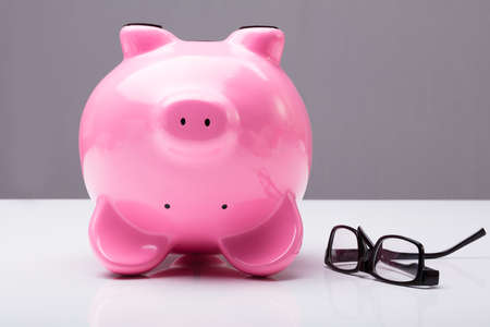 Close-up Of Upside Down Piggy Bank On Table With Eye Glasses On Deskの写真素材