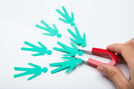 Close-up Of A Person's Hand Holding Red Horseshoe Magnet Attracting Paper Candidates On White Backgroundの写真素材