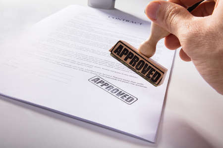 Close-up Of Person's Hand Stamping Approved On Contract Paperの写真素材