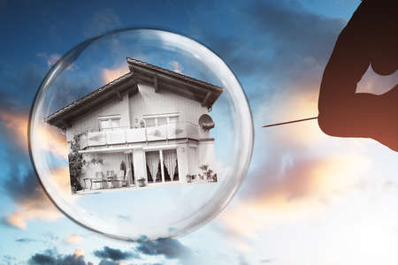Human Hand Poking House And Bubble With Needle Against Cloudy Skyの写真素材