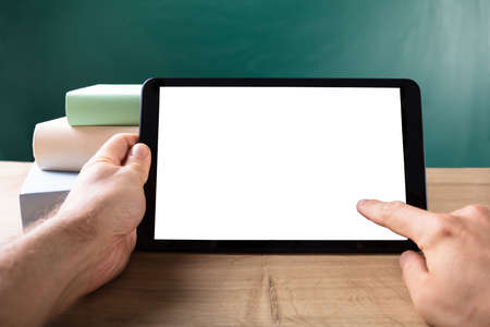 Human Hand With Digital Tablet Showing Blank White Screen In Front Of Blackboard
