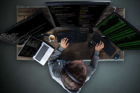 High Angle View Of Hacker Hacking Multiple Computers On Deskの写真素材