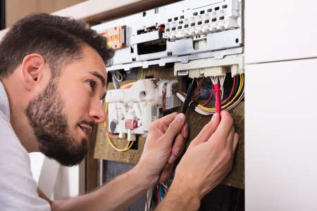 Male Technician Examining Dishwasher With Digital Multimeter