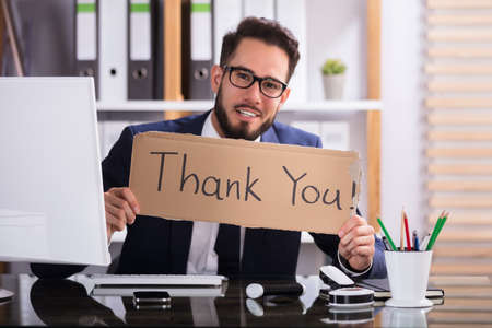 Smiling Young Businessman Holding Cardboard With Thank You Text In Officeの写真素材