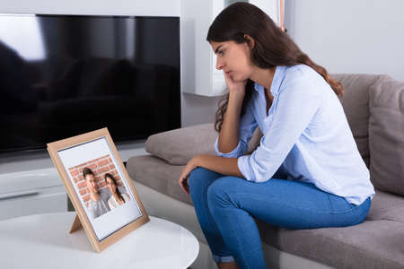Sad Woman Holding Picture Frame Of Couple In Love At Homeの写真素材