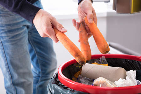 Close-up Of A Person's Hand Throwing Carrot In Dustbinの写真素材