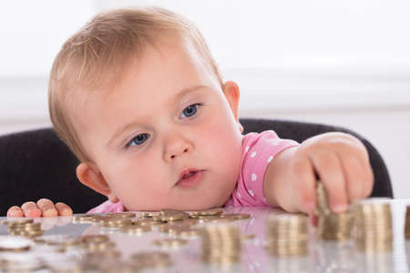 Close-up Of A Cute Little Baby Stacking Coins On Deskの写真素材