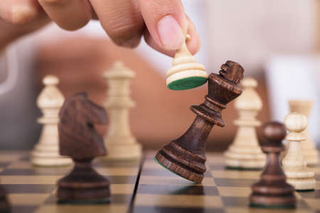 Close-up Of Hand Playing Chess And Falling King On Chess Boardの写真素材