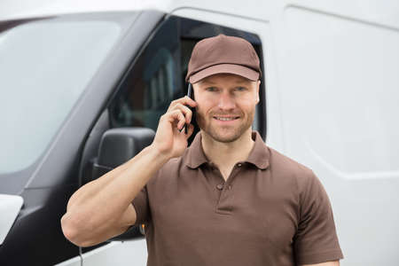 Close-up Of A Happy Young Delivery Man Talking On Mobile Phoneの写真素材