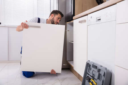 Young Handyman Fixing Sink Door In Kitchenの写真素材