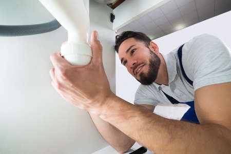 Happy Young Plumber Examining Sink Pipe In Kitchenの写真素材