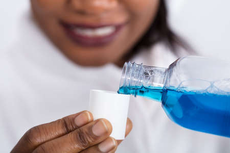 Close-up Of A Human Hand Pouring Mouthwash Into Bottle Capの写真素材