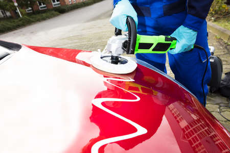 Close-up Of Person's Hand Polishing Car Hood With Orbital Polisher And Cleaner Compound