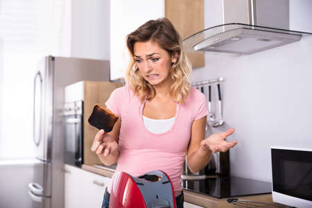 Young Unhappy Woman Removing Slices Of Burnt Toast From Toaster In Kitchenの写真素材