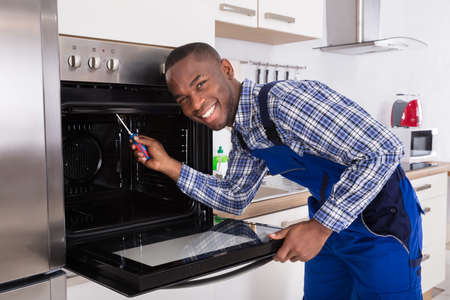 Young Repairman With Screwdriver Fixing Kitchen Ovenの写真素材