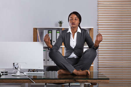 Young African Woman Sitting On Desk Meditating In Officeの写真素材
