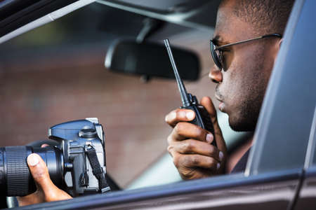Private Detective Sitting Inside Car Holding SLR Camera And Walkie Talkieの写真素材