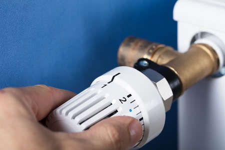 Person's Hand Adjusting Temperature On Thermostat To Control Heat In Central Heating System