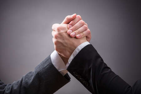 Close-up Of Two Businesspeople Competing In Arm Wrestling On Grey Backgroundの写真素材
