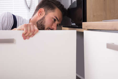Young Handyman Fixing Sink Door In Kitchenの写真素材