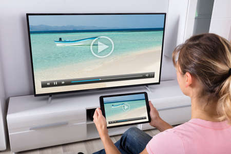 Young Woman Using Digital Tablet To Watching Television In Living Room