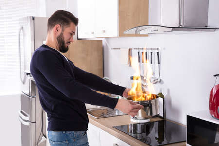 Side View Of A Young Man Holding Utensil On Fire In Kitchenの写真素材