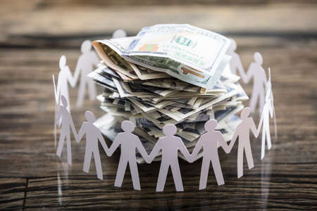Close-up Of Paper Cut Out Human Figure Surrounding Stacked Banknotes On Deskの写真素材
