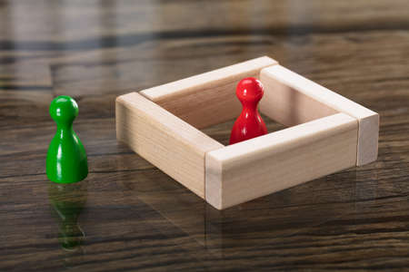 Red Figurine Pawn Surrounded By Wooden Blocks Besides Green Figurine Pawnの写真素材