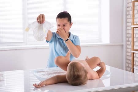 Mid Adult Woman Changing Stinky Diaper Of Her Baby On Desk At Homeの写真素材