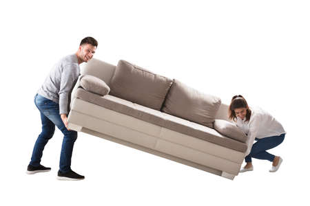 Happy Young Couple Lifting Sofa On White Backgroundの写真素材
