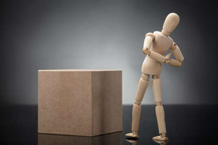 Wooden Dummy Standing Near Cardboard Box Suffering From Back Pain After Liftingの写真素材
