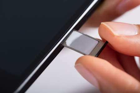 Close-up Of Person's Hand Inserting Micro Sim In Mobile Phoneの写真素材