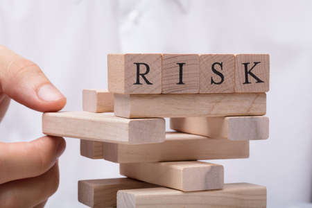 Person's Hand Removing Wooden Block From Tower With Risk Word On Topの写真素材