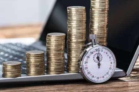 Close-up Of Stopwatch With Increasing Stacked Coins On Laptop
