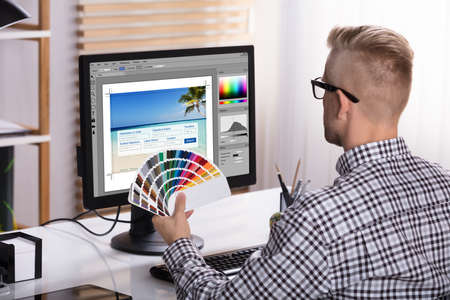 A Male Designer Using Computer While Holding Color Swatches In His Handの写真素材