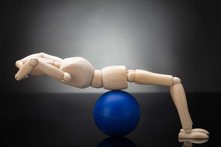 Side View Of A Wooden Dummy Doing Workout On Fitness Ball Against Grey Backgroundの写真素材