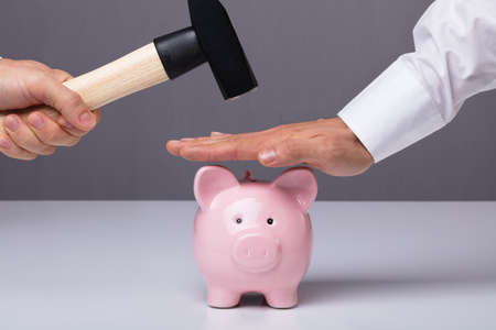 Close-up Of Businessman's Hand Saving Piggybank From Hammeringの写真素材