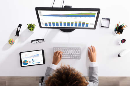 Elevated View Of A Businesswoman Analyzing Graph On Computer At Workplace