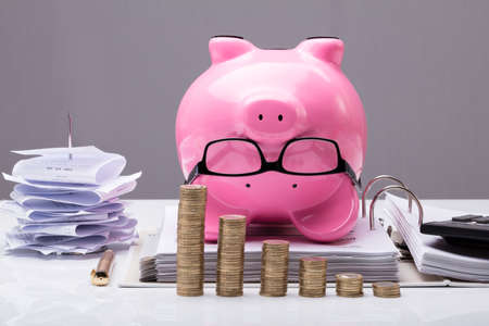 Close-up Of Stacked Coins In Front Of Upside Down Piggy Bank On Documents In Officeの写真素材