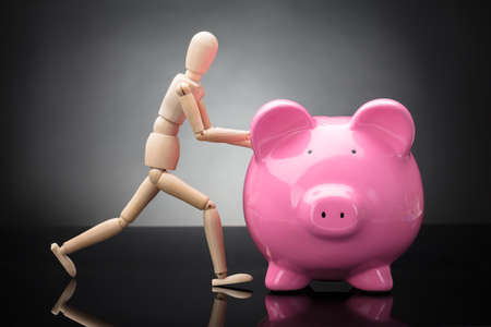 Side View Of A Wooden Dummy Holding Pink Piggy Bankの写真素材