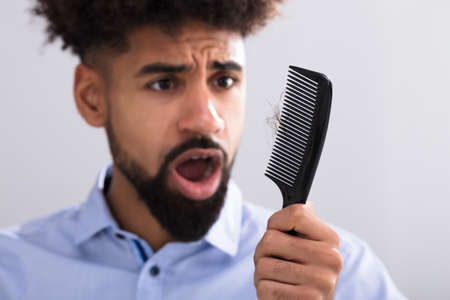 Young Man Holding Comb Looking At Hair Loss